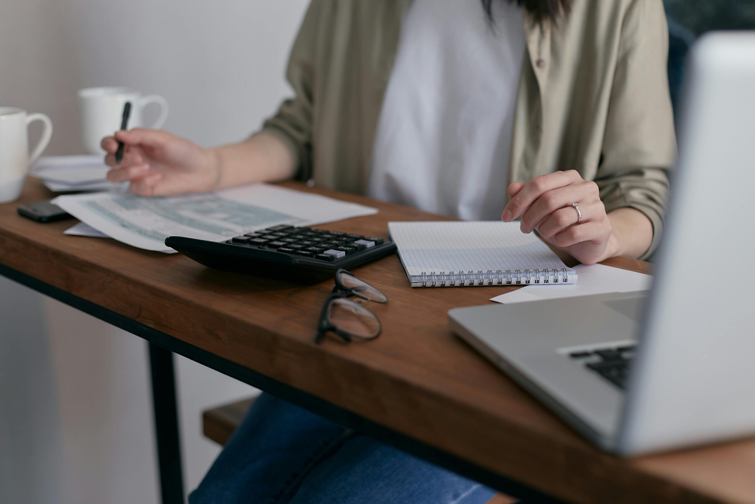 Person reviewing financial documents with a calculator and laptop, planning short-term commercial loans for business expenses.