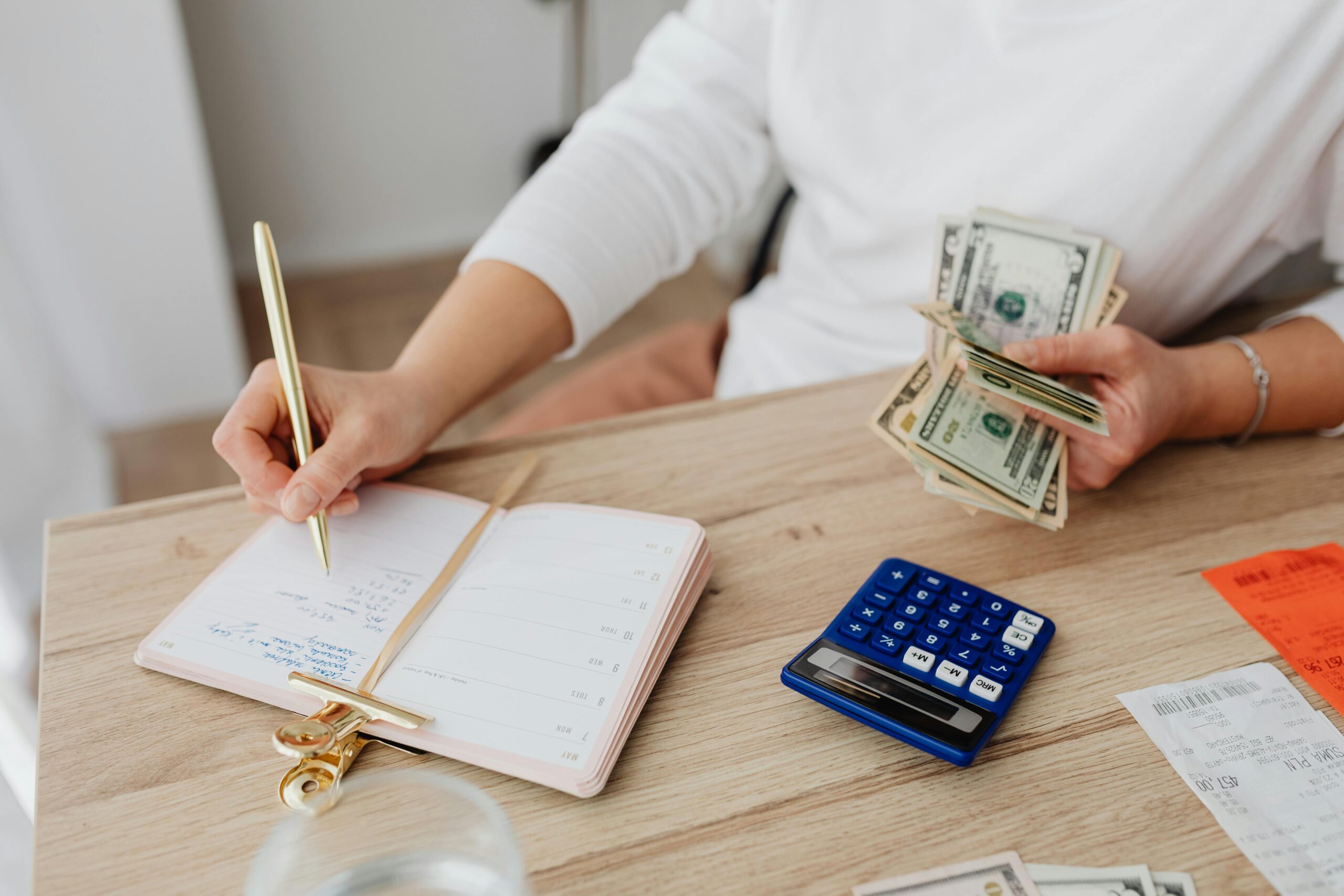 A person managing finances with cash, a notebook, and a calculator on a desk—demonstrating the need to increase credit score for SBA loan approval.