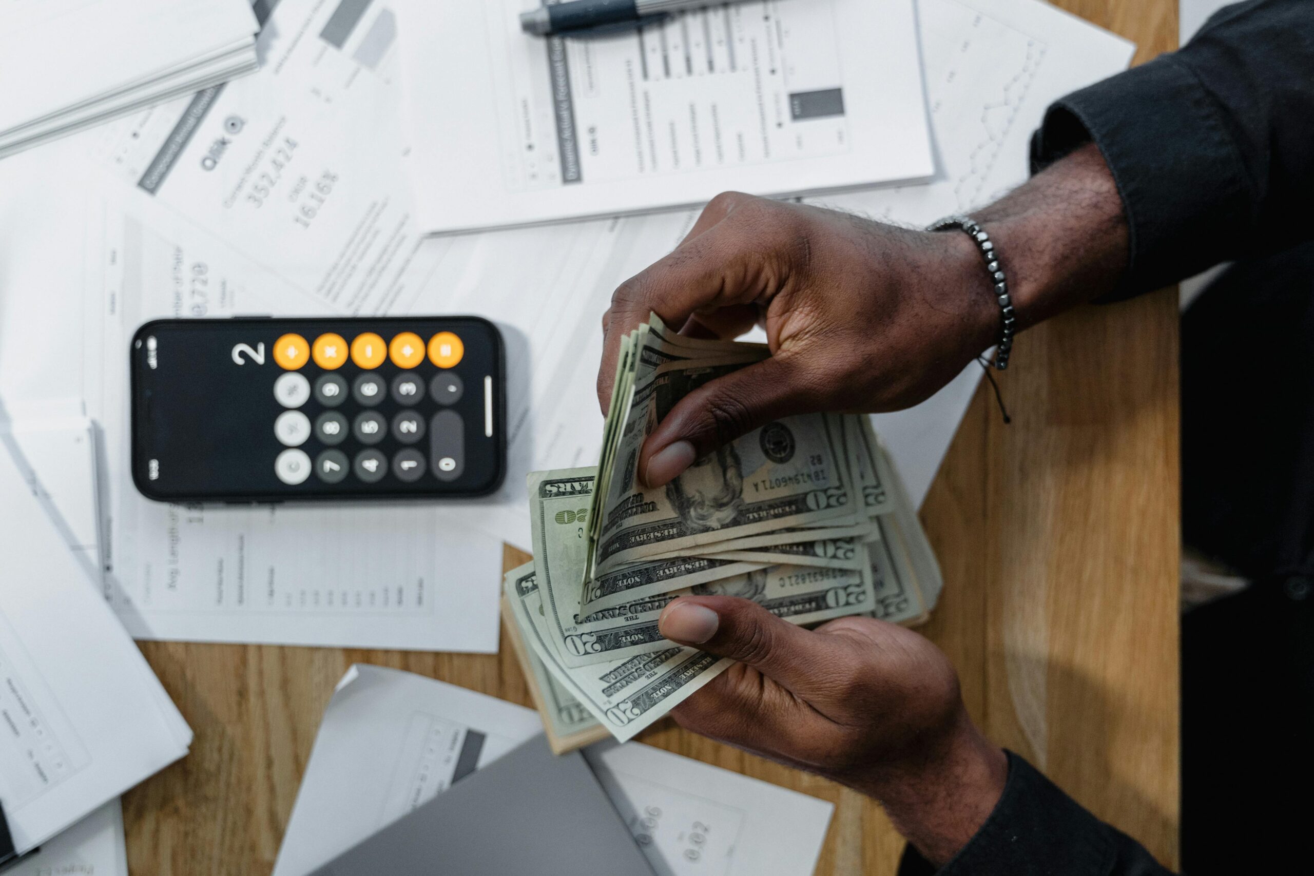 Close-up of cash being counted over business reports, symbolizing the impact of business & financial solutions on cash flow.