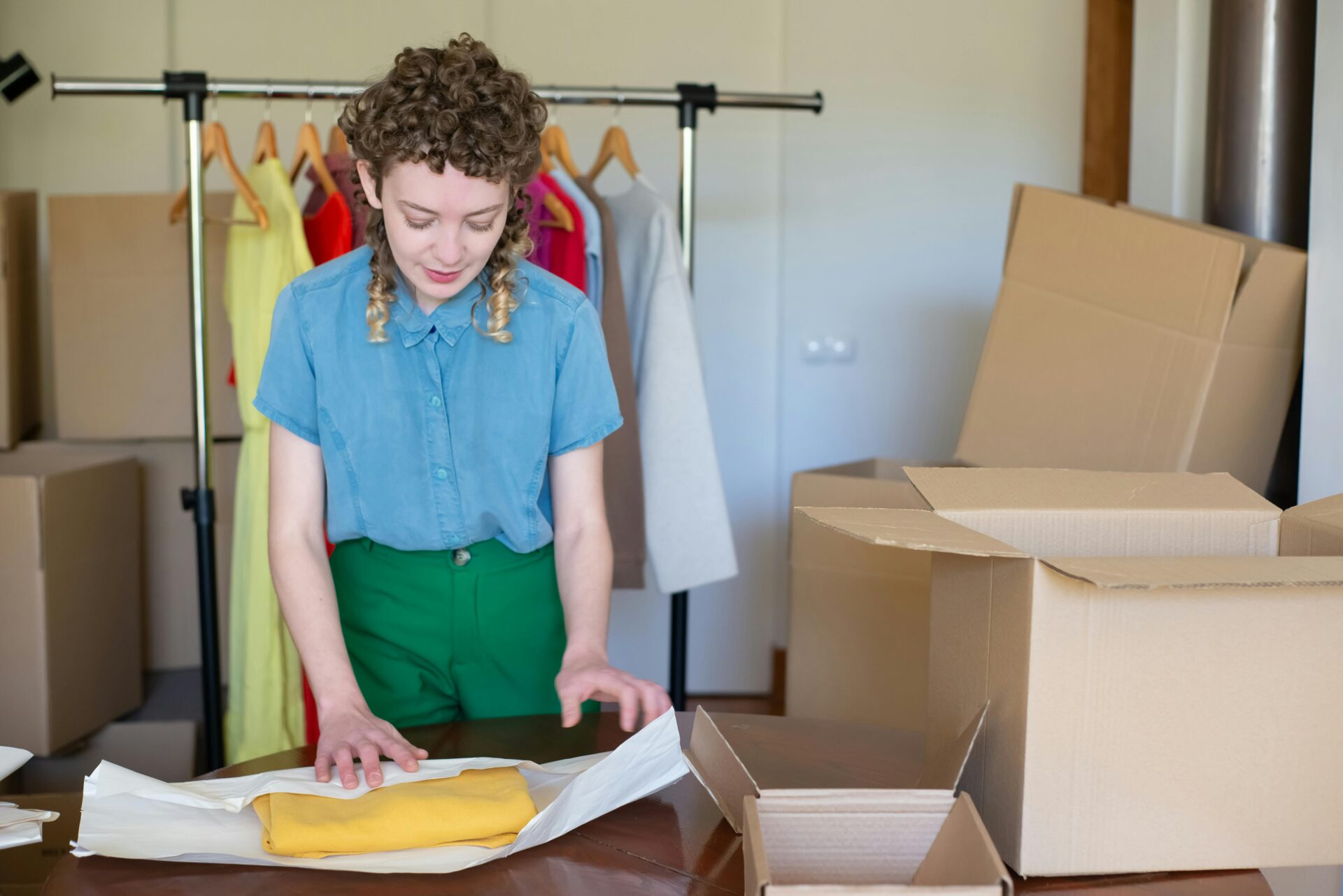 A small business owner packing clothes for shipment, surrounded by boxes, showing the real-world tariff impact on small businesses in retail.