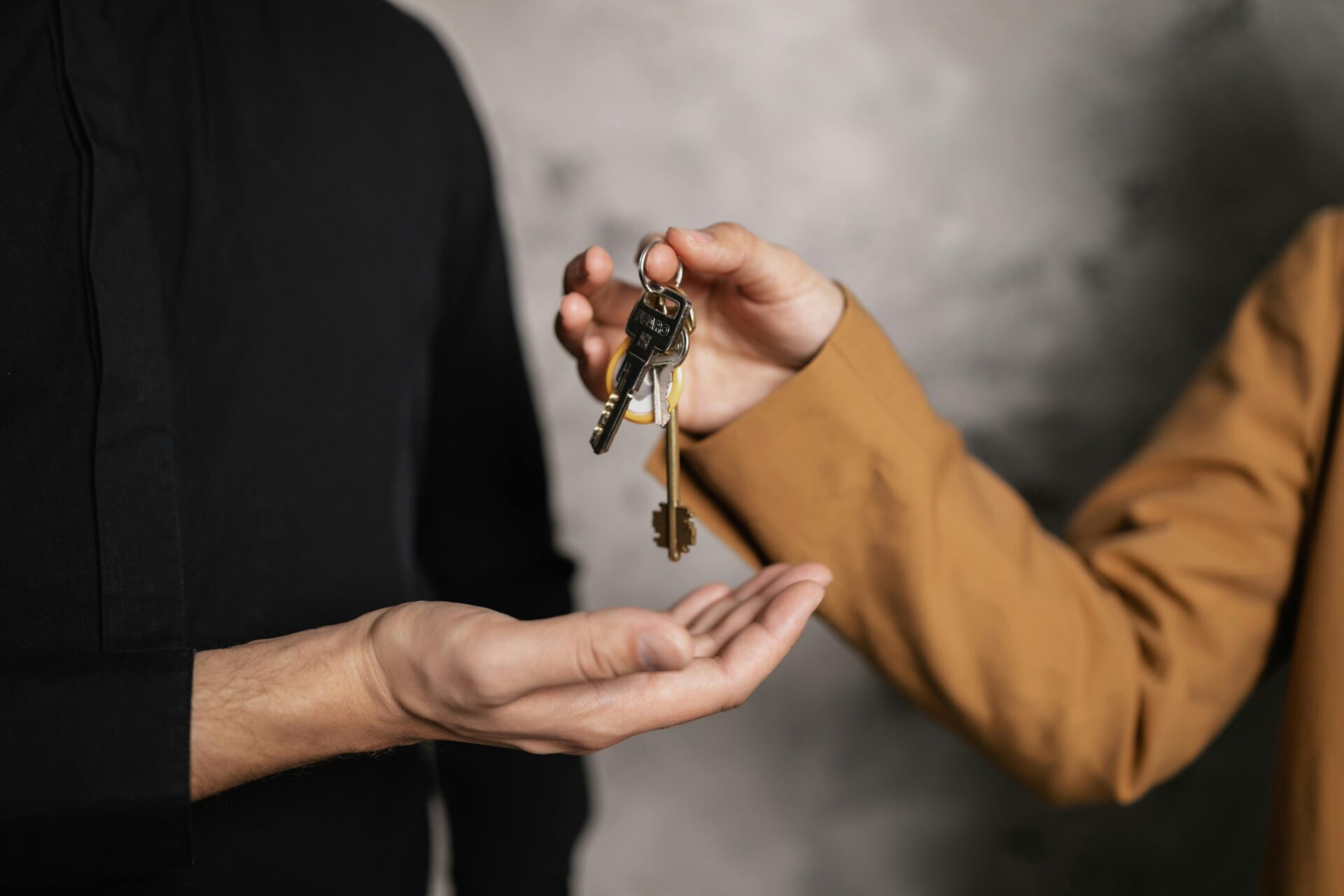 A close-up of a hand passing a set of brass keys to another person, symbolizing the successful closing of commercial real estate loans