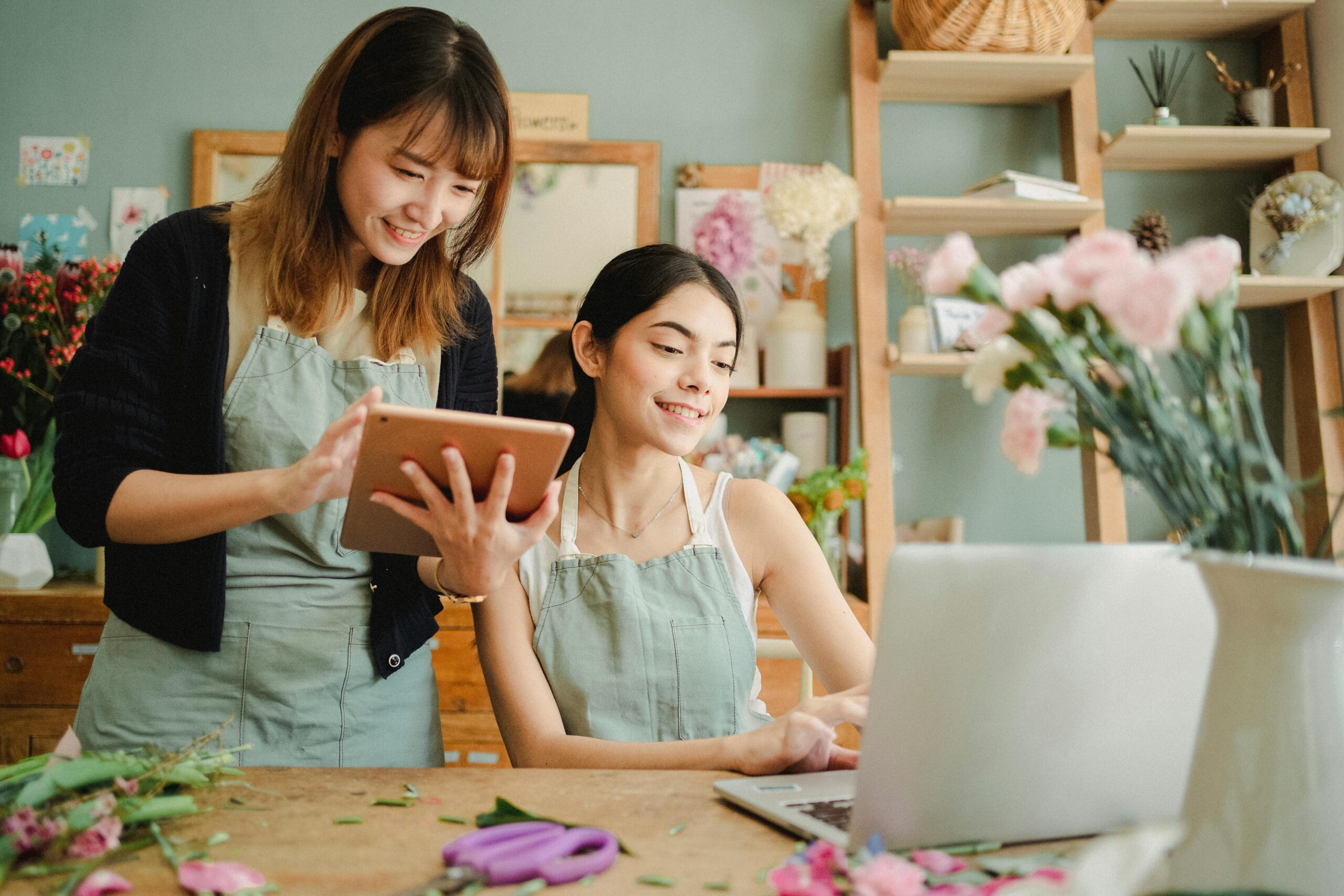 Small business owners reviewing plans on a tablet while arranging flowers, discussing business expansion financing options.