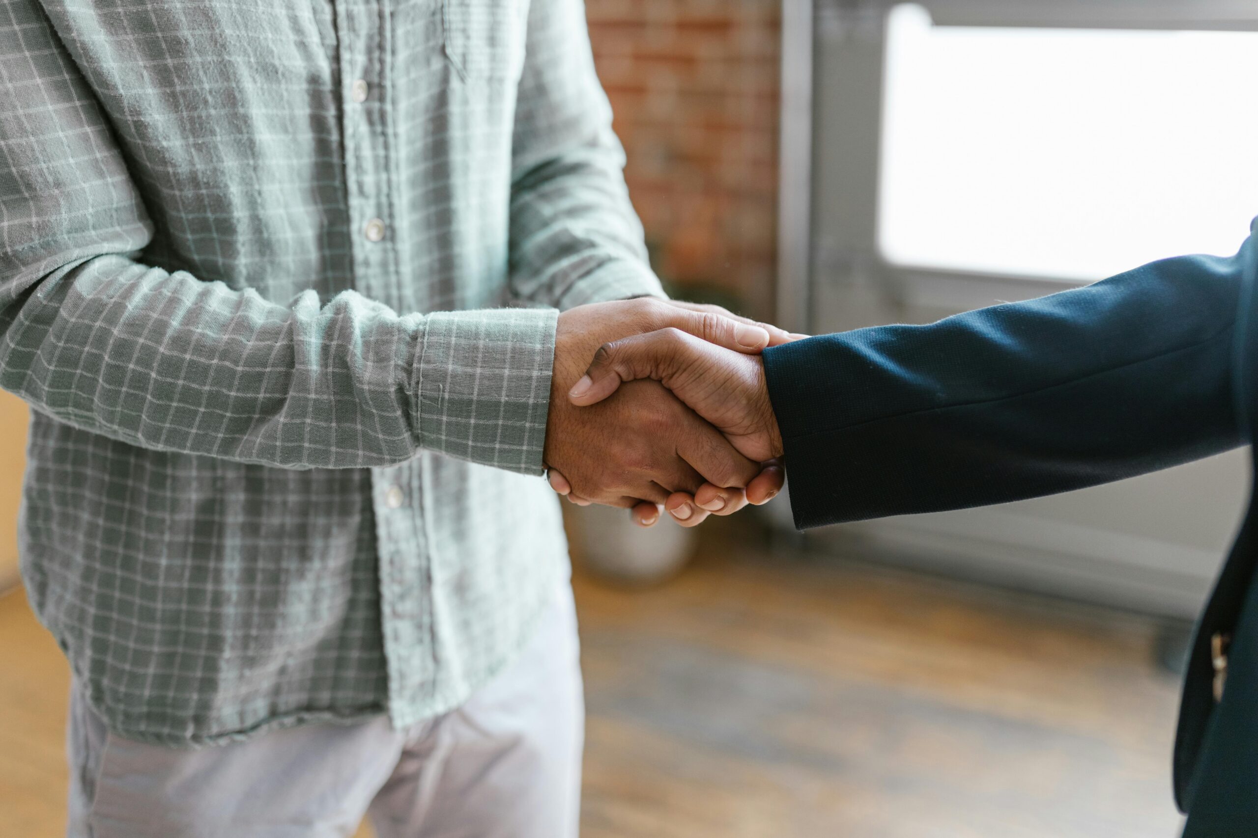 A close-up of two people shaking hands in a bright office to finalize a deal for a business owner retiring and selling their company.