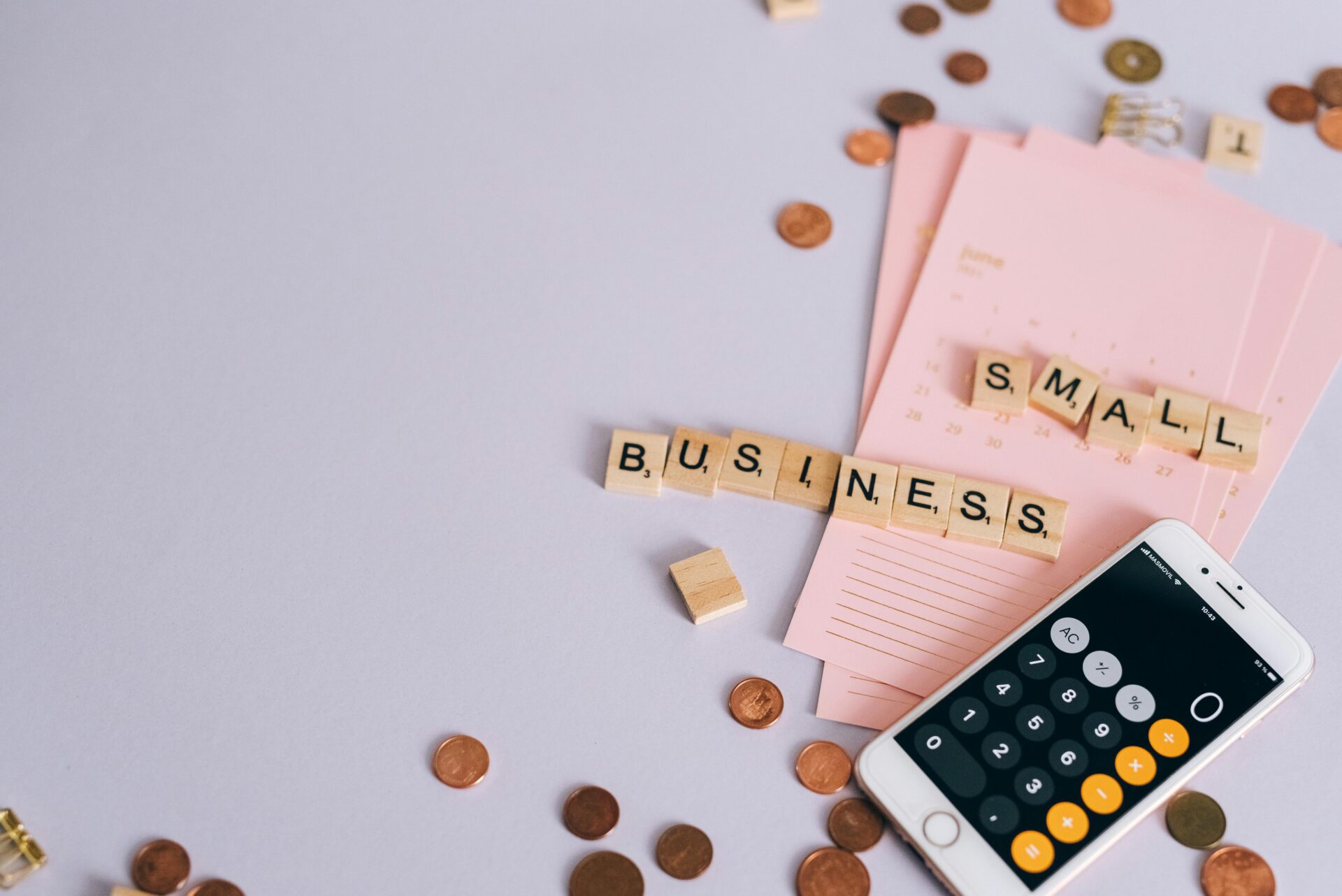 Wooden tiles spelling out "Small Business" on a pink desk calendar, perfect for planning small business month growth strategies.